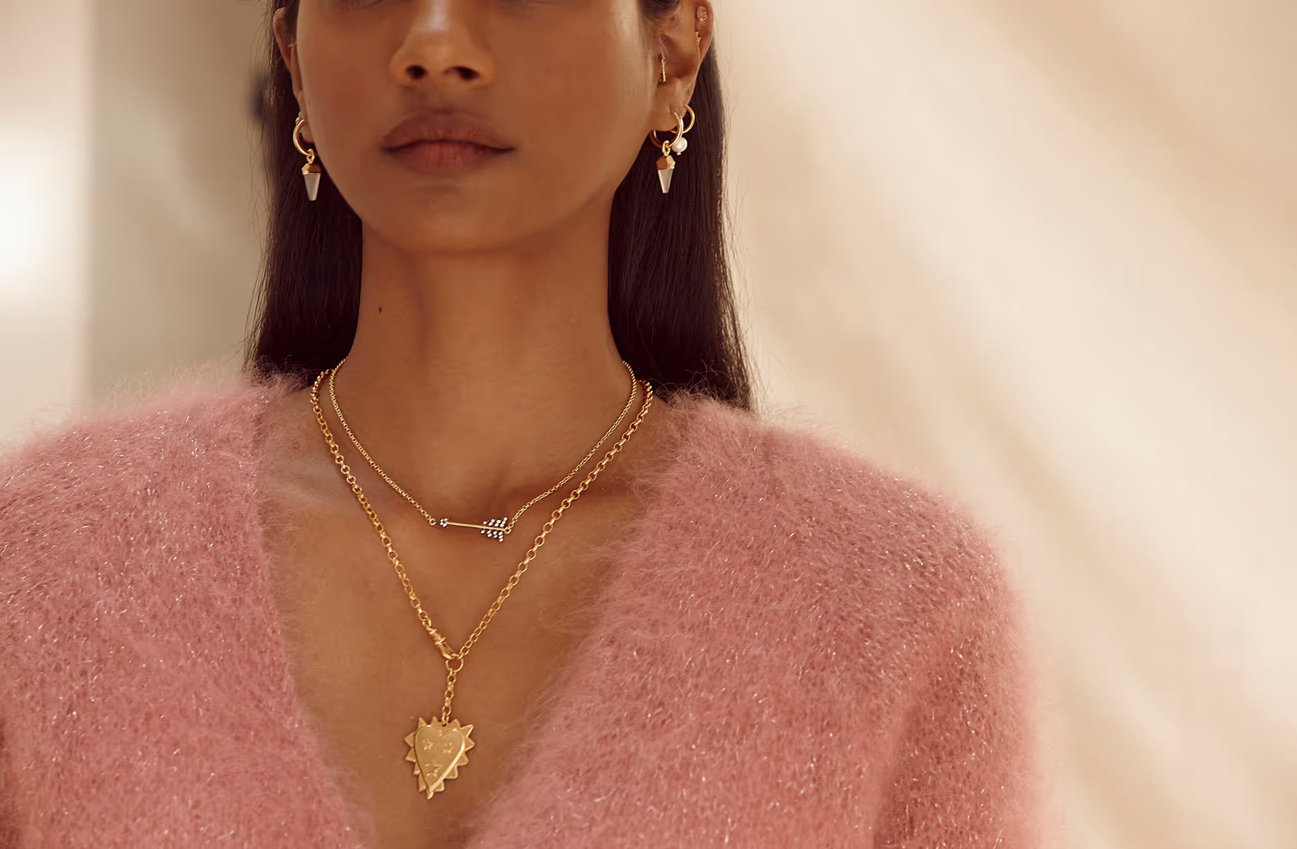 A woman in a pink fluffy jumper wearing Harry Rocks necklaces and earrings